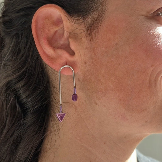 Close-up of a person wearing a silver earring with a purple ceramic pieces.
